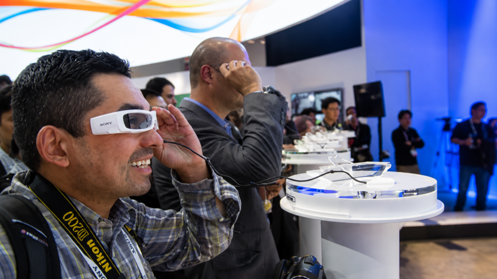 A man smiling while trying on smart glasses at a technology product display stand.