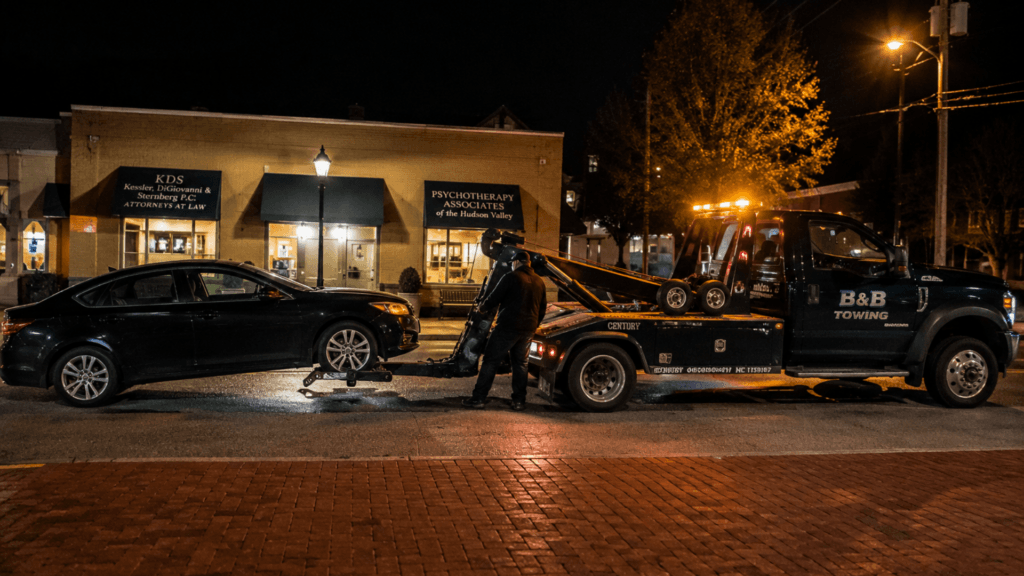 A B&B Towing truck hooking up a black sedan on a city street at night.