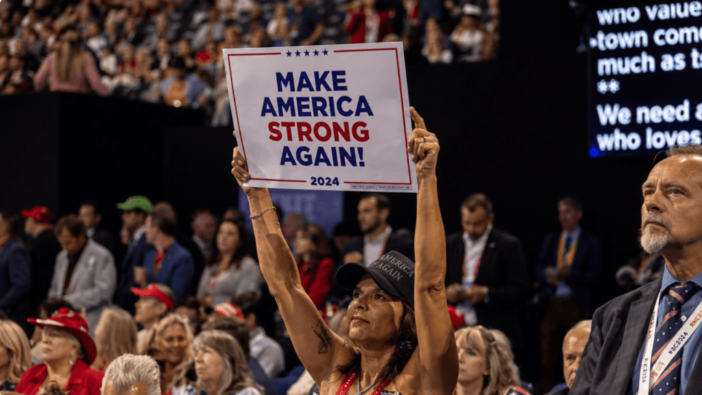 A woman holding a "Make America Strong Again!" sign at a 2024 campaign rally.