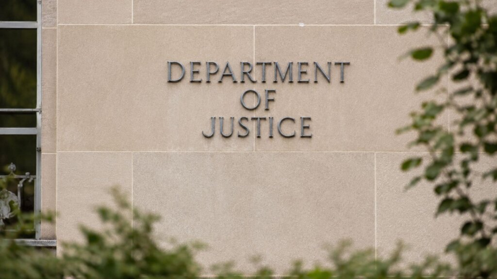 Exterior wall of the Department of Justice building with the words "DEPARTMENT OF JUSTICE" displayed in large metal letters.