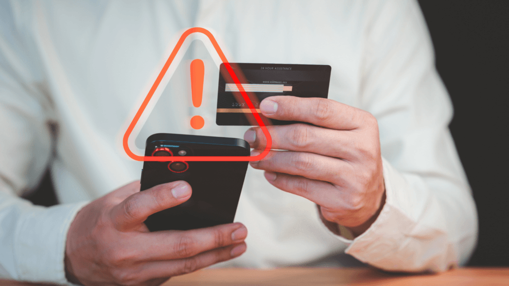 A person holding a smartphone and a credit card, with a glowing red warning triangle overlay.