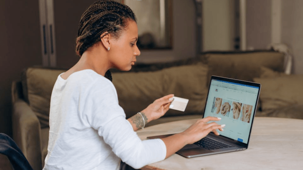 A woman sitting at a table, holding a credit card while looking at a laptop.