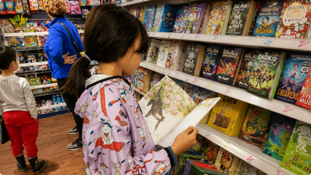 Child reading a picture book in a bookstore aisle.