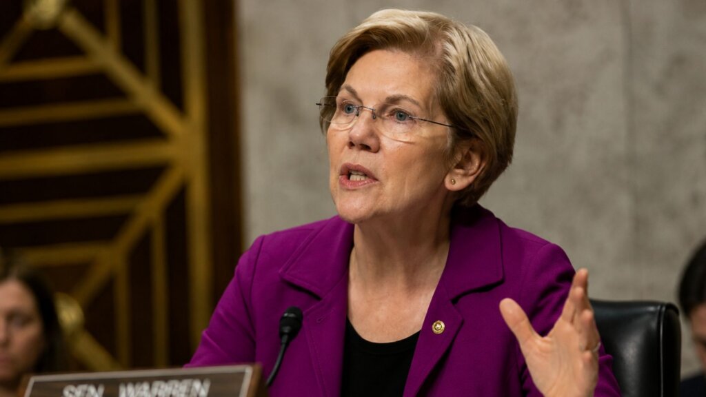 Senator Elizabeth Warren, wearing a purple blazer, speaks into a microphone during a government hearing while gesturing with one hand.