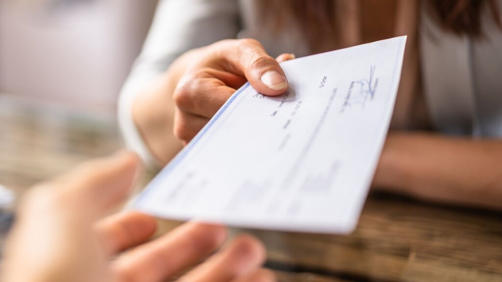 Close up of a person handing a check to another person across a table.