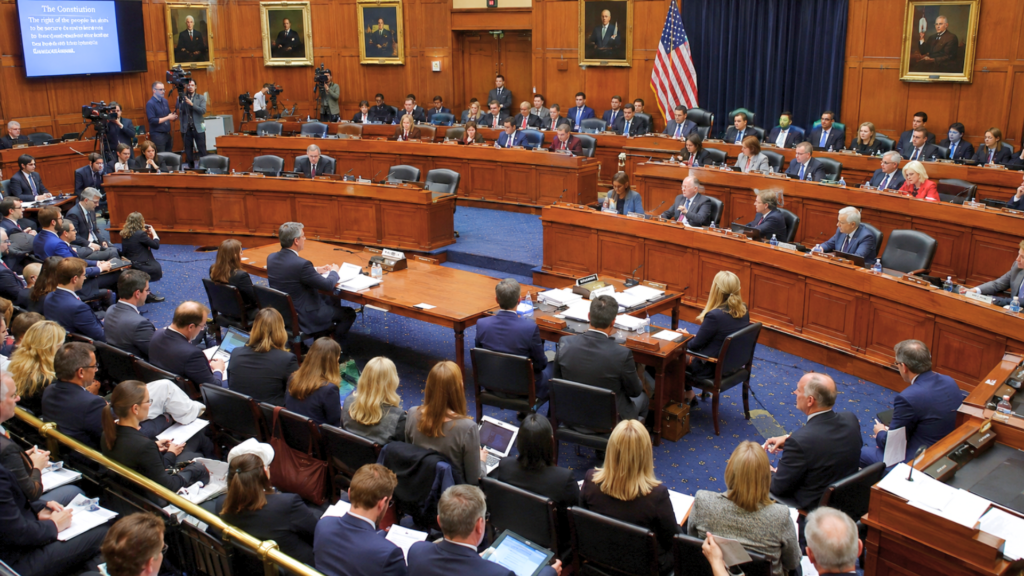 Lawmakers and officials conducting a congressional committee hearing inside a wood-paneled government chamber.