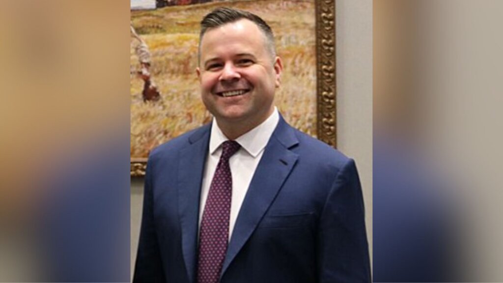 Federal Housing Finance Agency Director Bill Pulte, in a blue suit and patterned tie, stands indoors in front of a framed landscape painting.