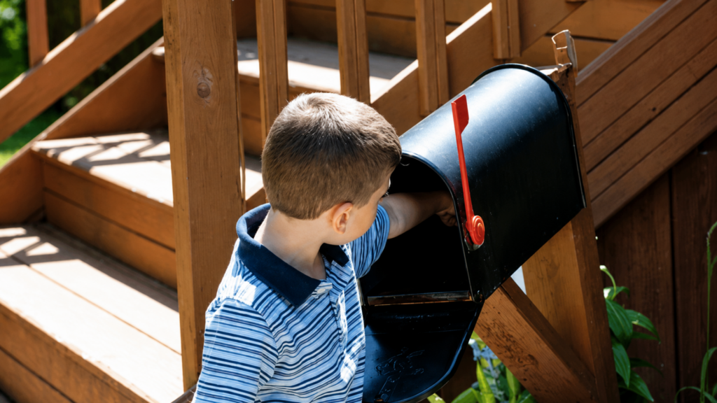 Boy reaching into a black mailbox outside a home.