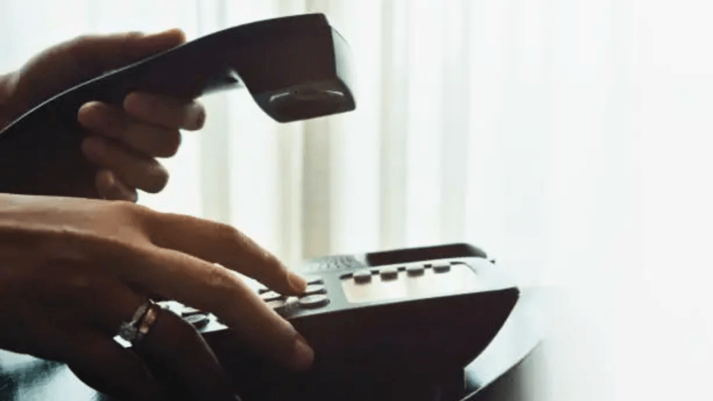 Person dialing a number while holding a landline phone receiver.