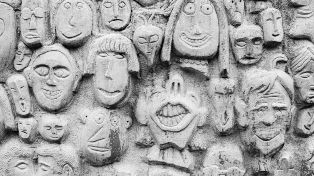 Stone wall covered with carved faces showing varied expressions.