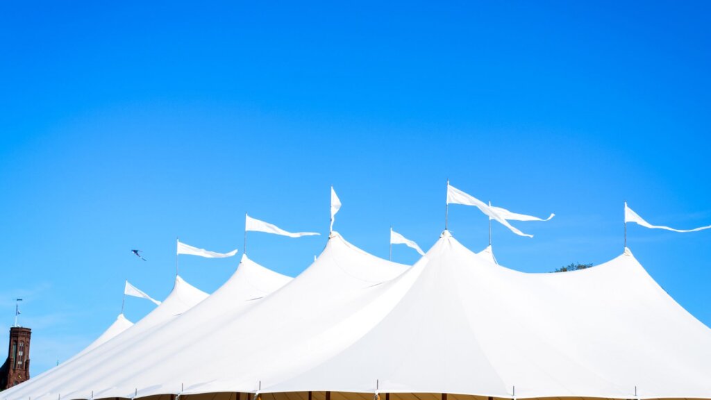 Large white event tent with flags against a bright blue sky.