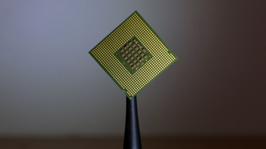 A close-up shot of a green silicon semiconductor microprocessor chip held vertically by a pair of black tweezers.