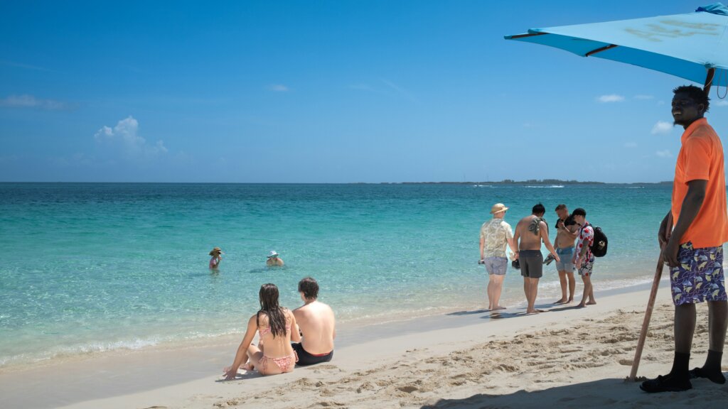 Beachgoers relax and wade in the clear turquoise waters of a beach in Nassau, Bahamas