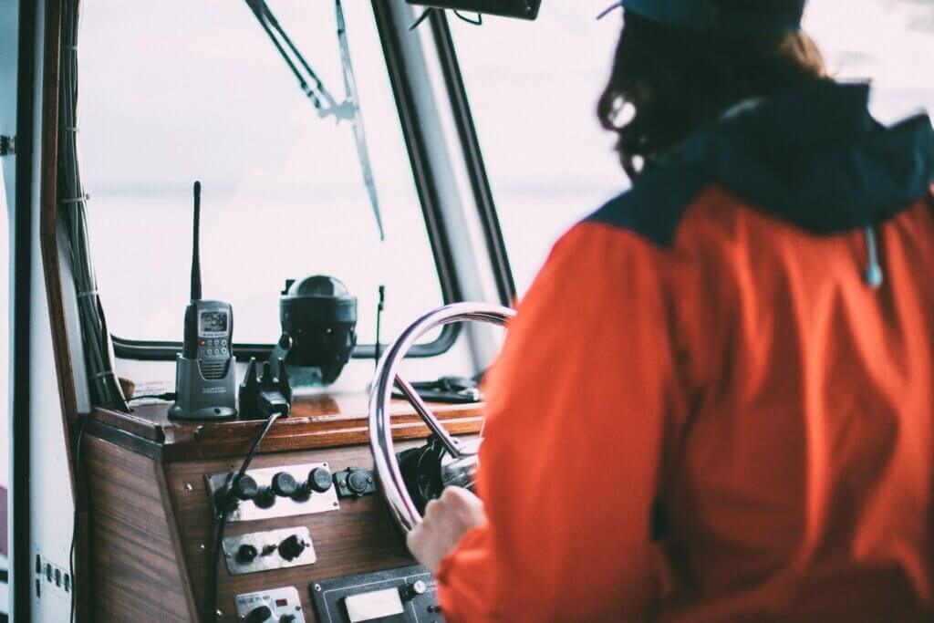 Boat operator steering a vessel from the helm inside the cabin.