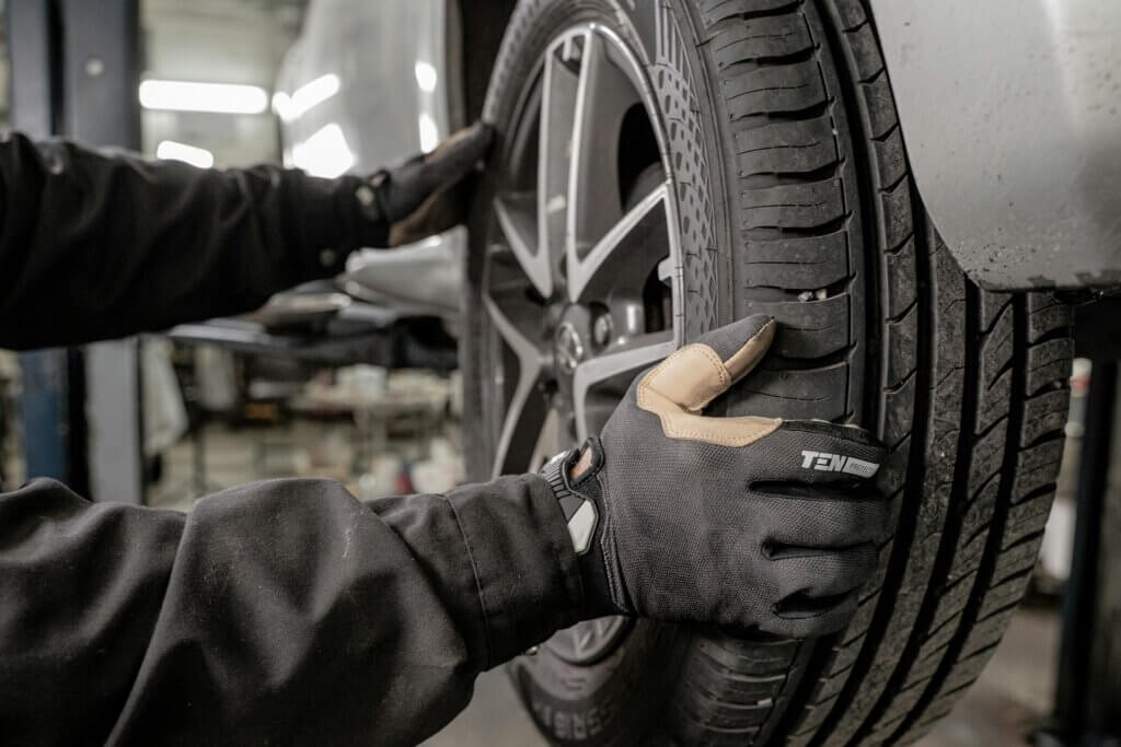 Technician inspecting tire tread on a vehicle wheel during a maintenance check at an automotive service center.