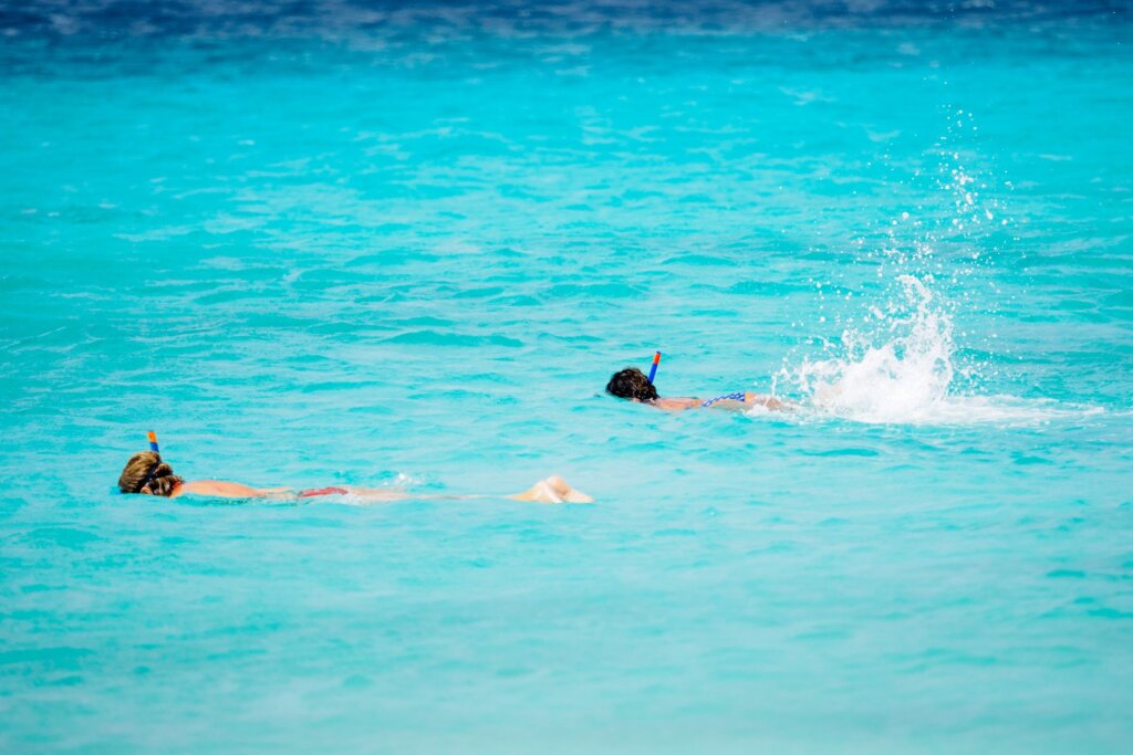Two people snorkel in shallow turquoise water.