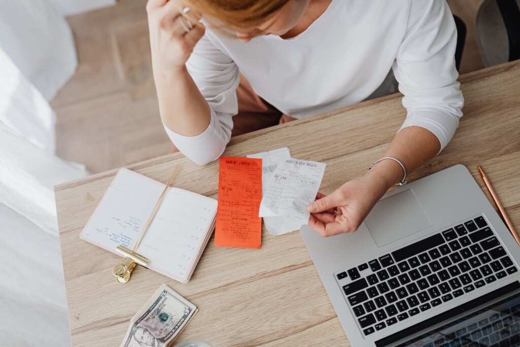 Woman examining receipts and expenses beside a laptop at home.