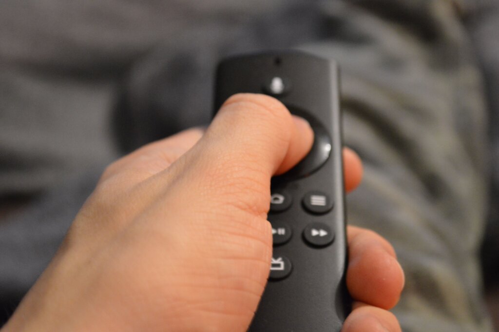 Hand holding a streaming device remote control while navigating entertainment content on a television.