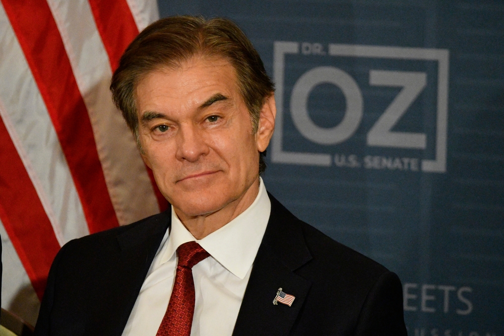 CMS Administrator Dr. Mehmet Oz appears at a public event with a U.S. Senate campaign backdrop and American flag.