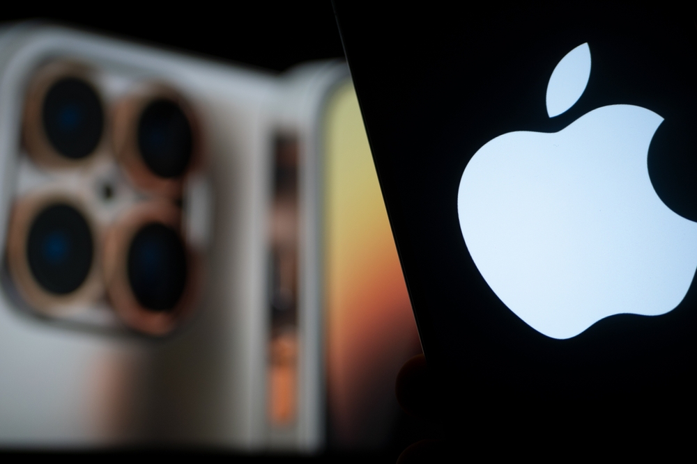 Apple logo displayed on a smartphone screen with an iPhone shown out of focus in the background.