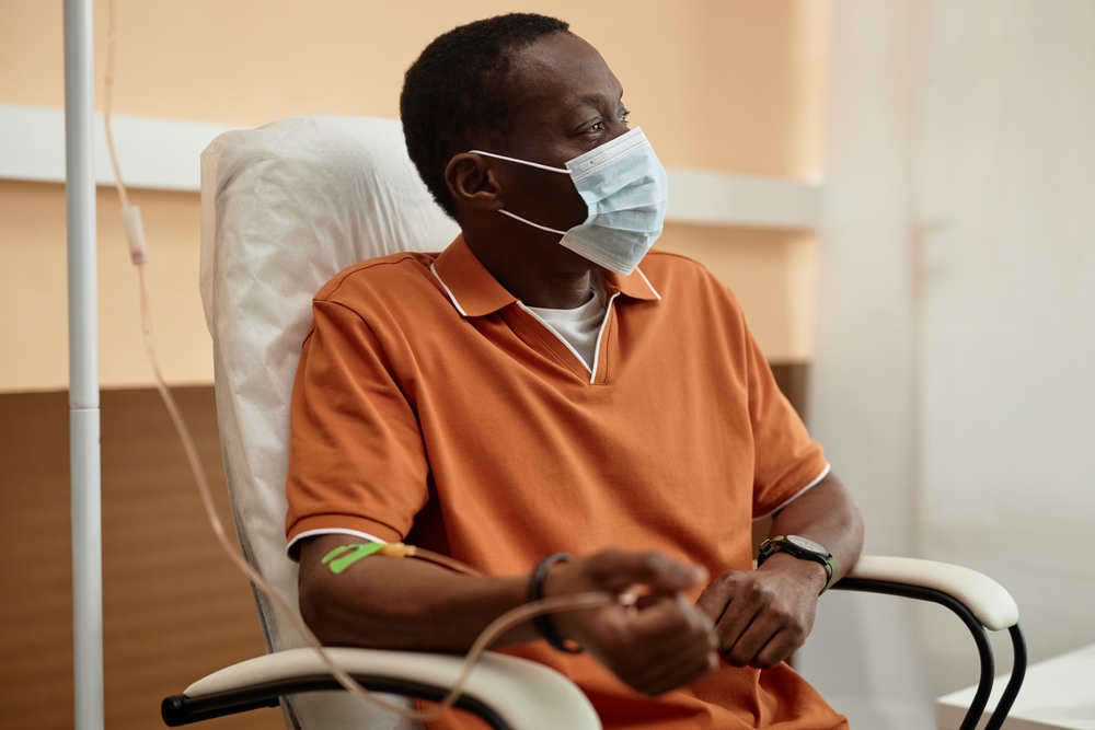 Patient wearing a face mask receives intravenous treatment while seated in a healthcare facility.