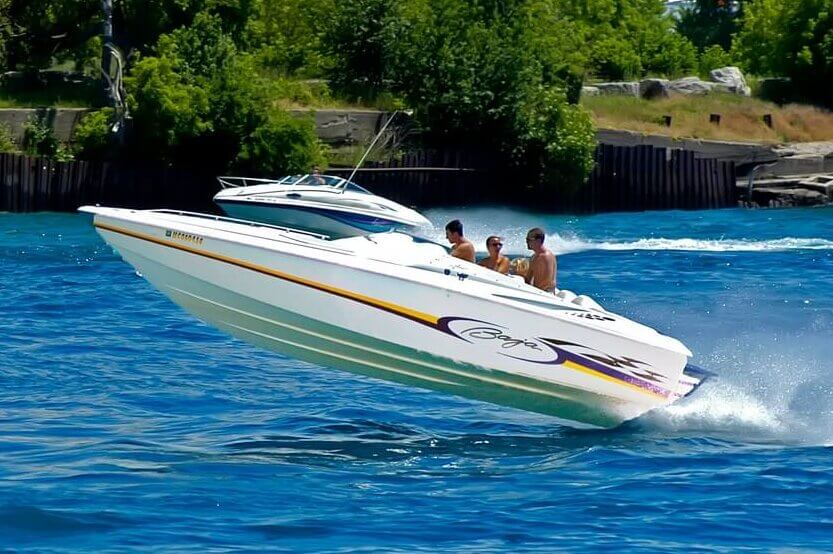 Speedboat carrying passengers races across a waterway near a shoreline.