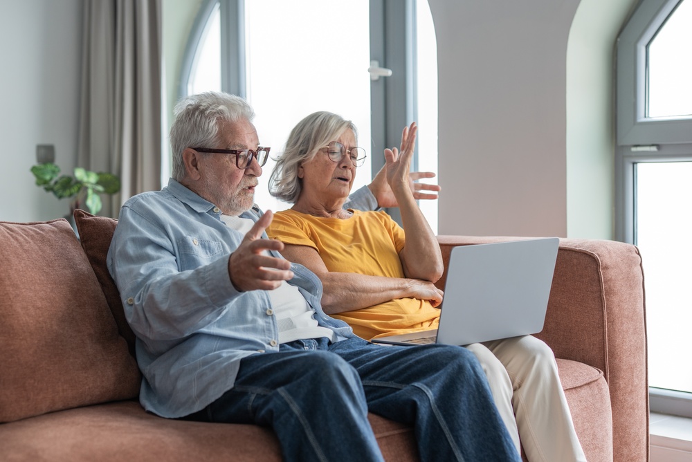 Older couple sitting on a couch looking at a laptop with concerned expressions and gestures.