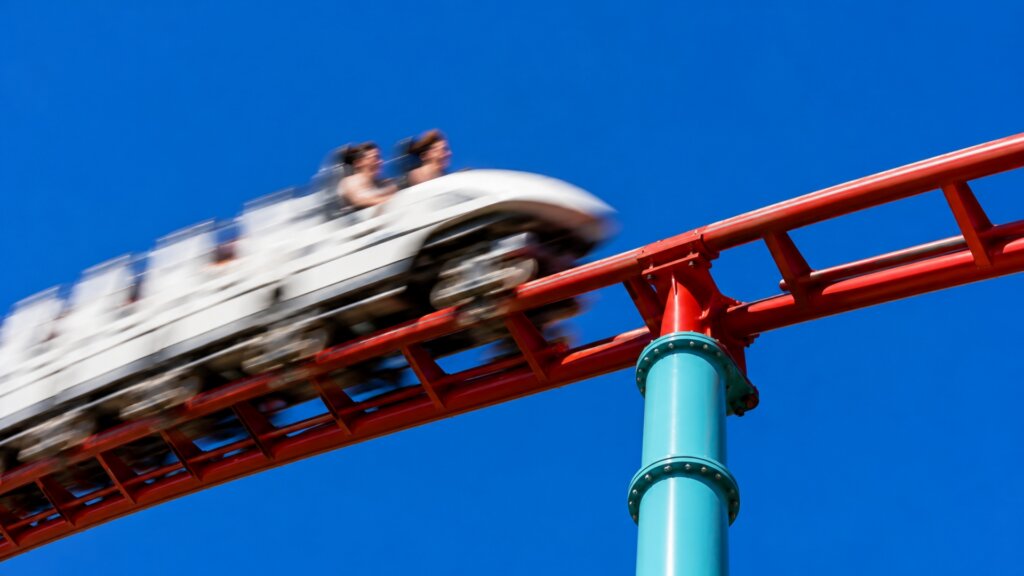 Motion blurred roller coaster train racing along bright red track against a deep blue sky.