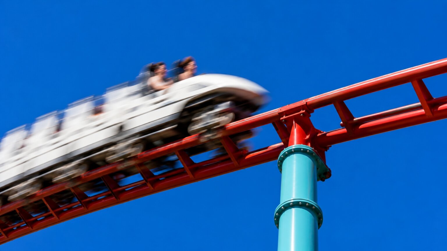 Motion blurred roller coaster train racing along bright red track against a deep blue sky.