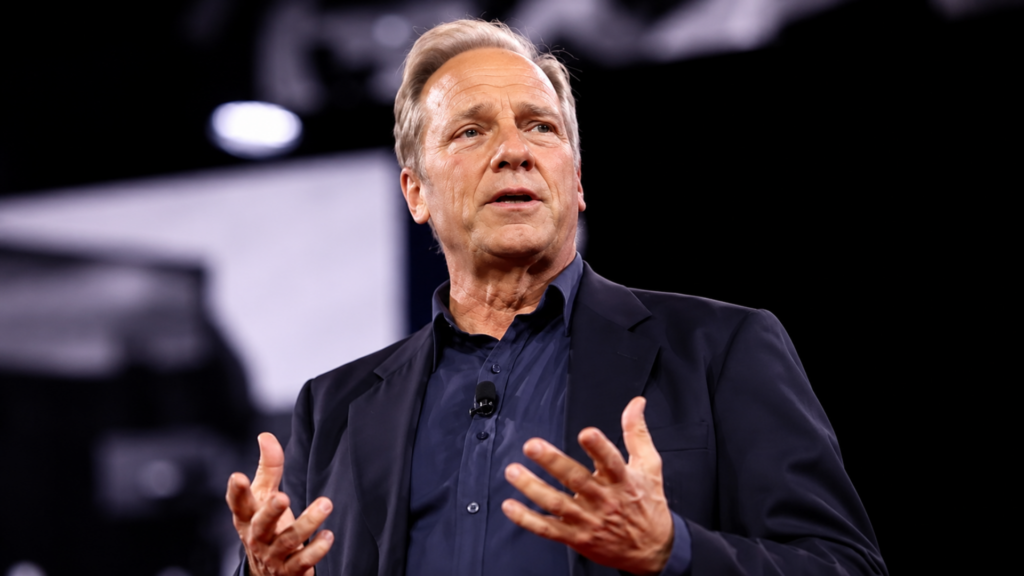 Mike Rowe speaking on stage during a public event or conference presentation.