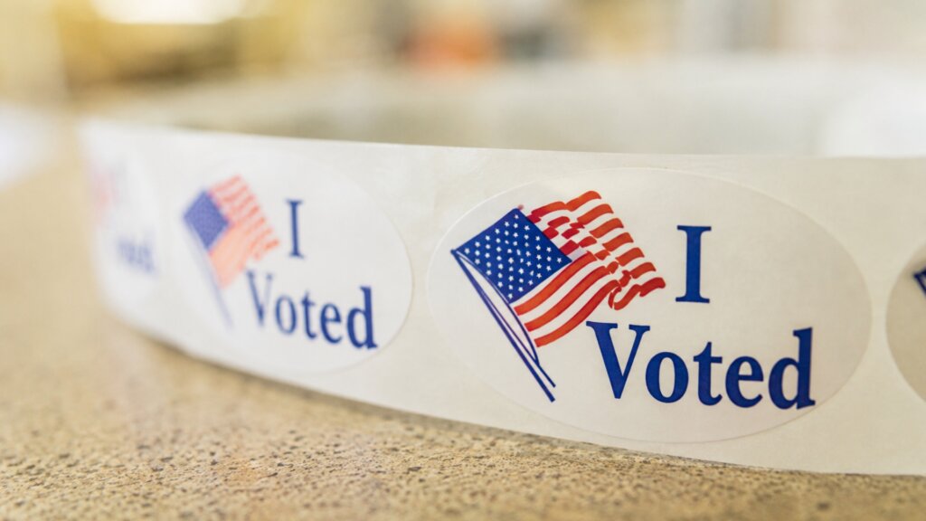 Roll of oval "I Voted" stickers featuring a waving American flag resting on a countertop.