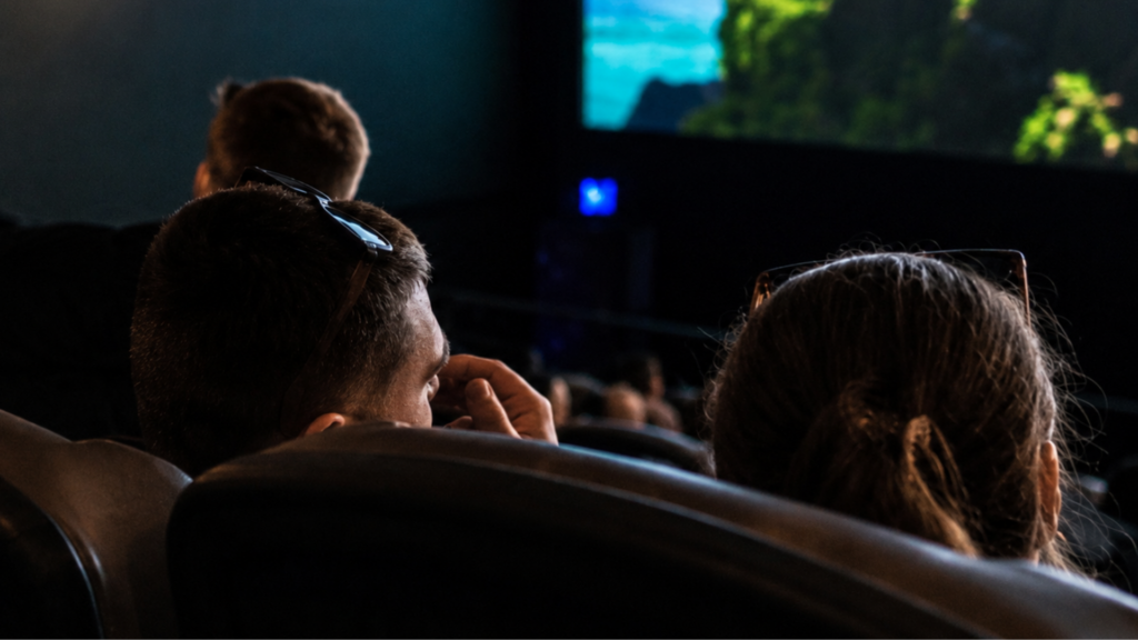 Rear view of moviegoers sitting in a theater watching a film on a large screen.