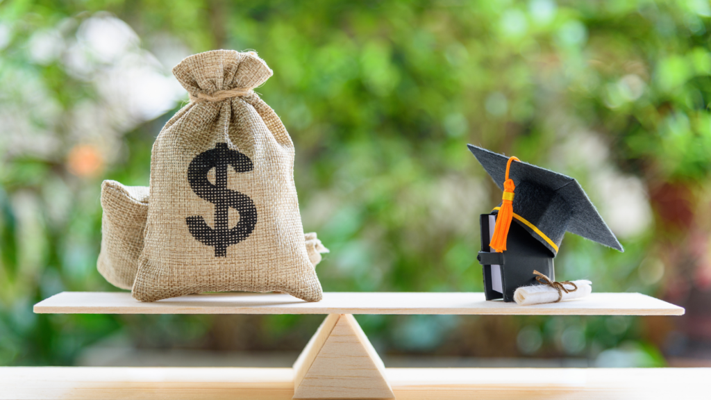 A wooden balance scale weighing a burlap sack with a dollar sign against a miniature graduation cap, book, and diploma.