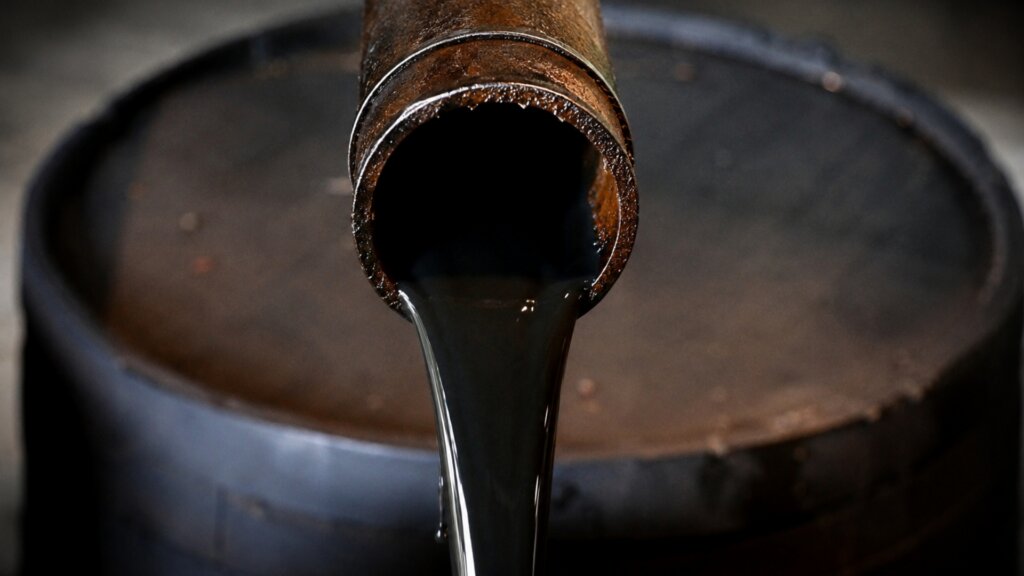 Thick black liquid pours from a metal pipe into a large industrial container.