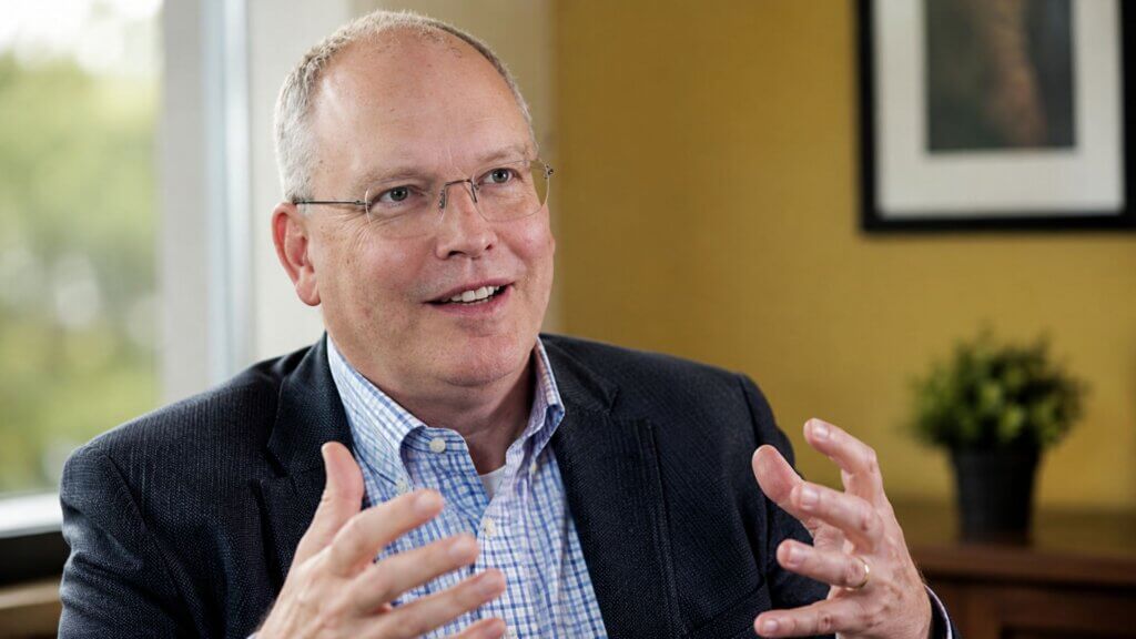 Phil Koopman, in a business suit, gestures with both hands while speaking during an interview in an office setting.