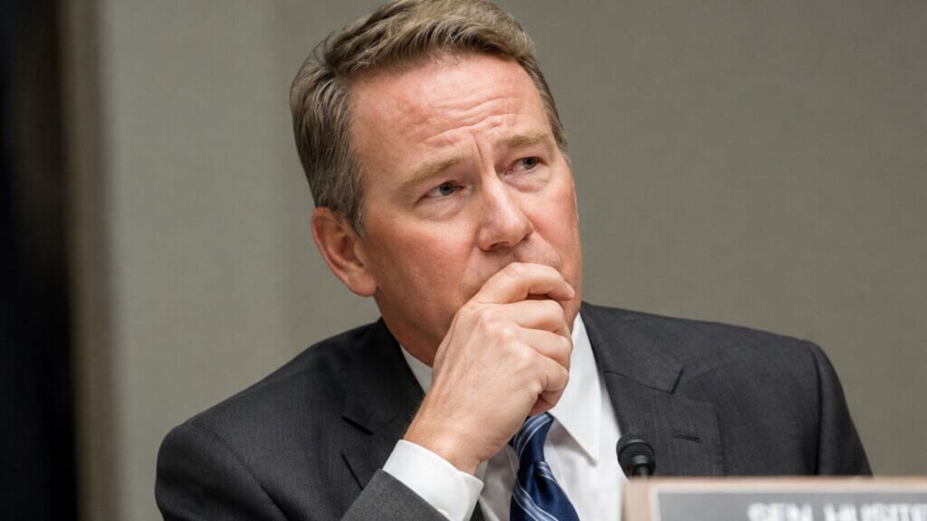 Sen. Jon Husted sits with his hand resting against his chin during a congressional hearing, appearing to listen intently.