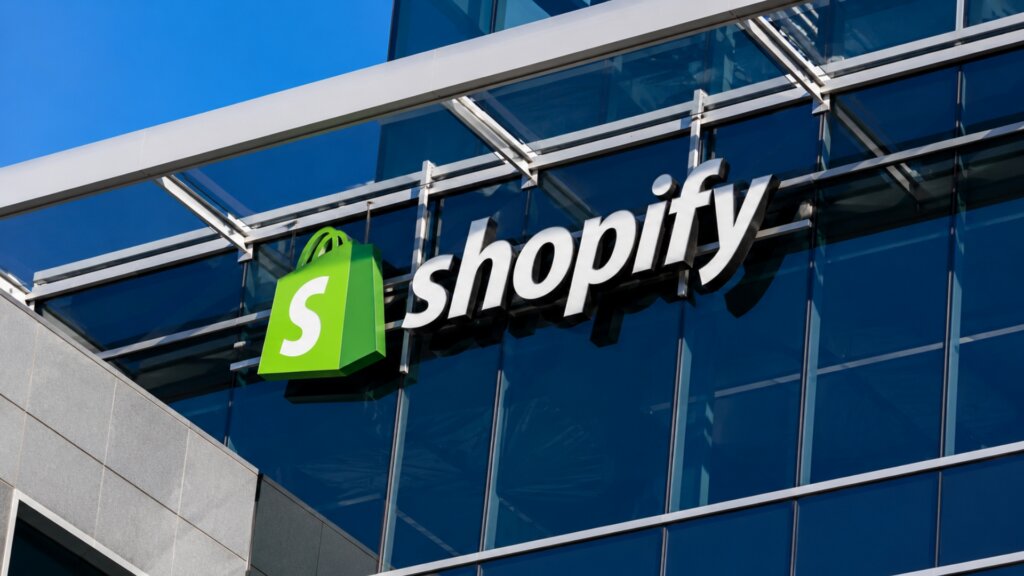 Shopify logo displayed on the glass exterior of a modern office building beneath a clear blue sky.