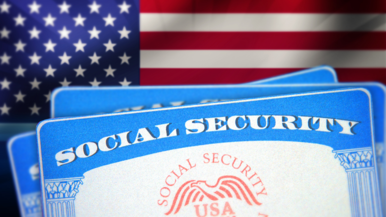 A close-up of a blue and white U.S. Social Security card in front of a blurry American flag.