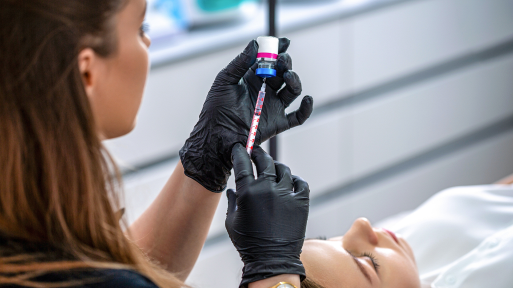 A healthcare professional wearing black gloves drawing medication from a small vial into a syringe.