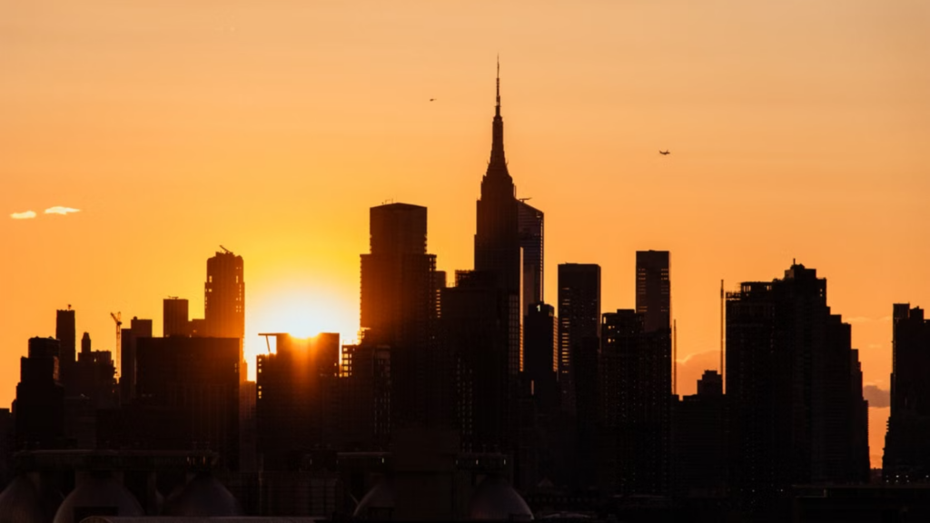 The dark silhouette of a city skyline against a bright orange sunset.