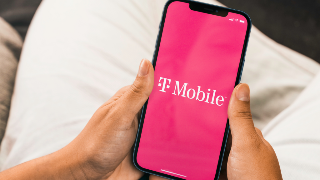 A close-up of a person's hands holding a smartphone displaying the pink T-Mobile logo on its screen.
