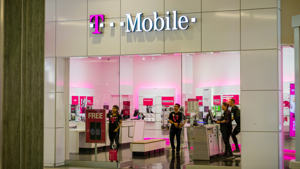 The brightly lit storefront of a T-Mobile retail store inside a shopping mall with employees visible inside.
