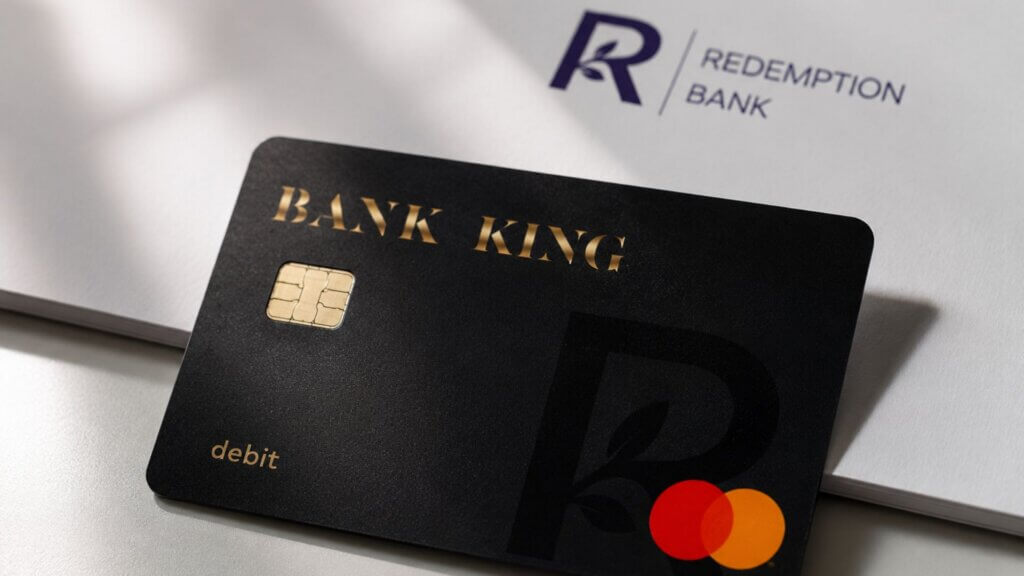A black debit card labeled "BANK KING" rests on top of a folder displaying the Redemption Bank logo.