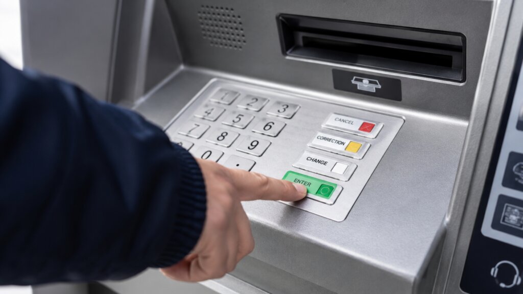 A person presses the green "ENTER" button on an ATM keypad beneath the card slot.