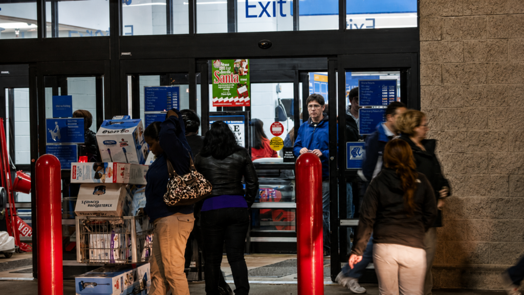 Shoppers entering and exiting through the automatic glass doors of a store entrance.