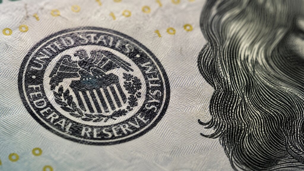 Close up of the United States Federal Reserve seal printed on U.S. currency beside part of a portrait.