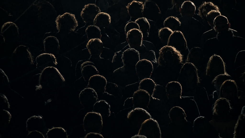 Silhouettes of a large crowd of people seated inside a dark theater.