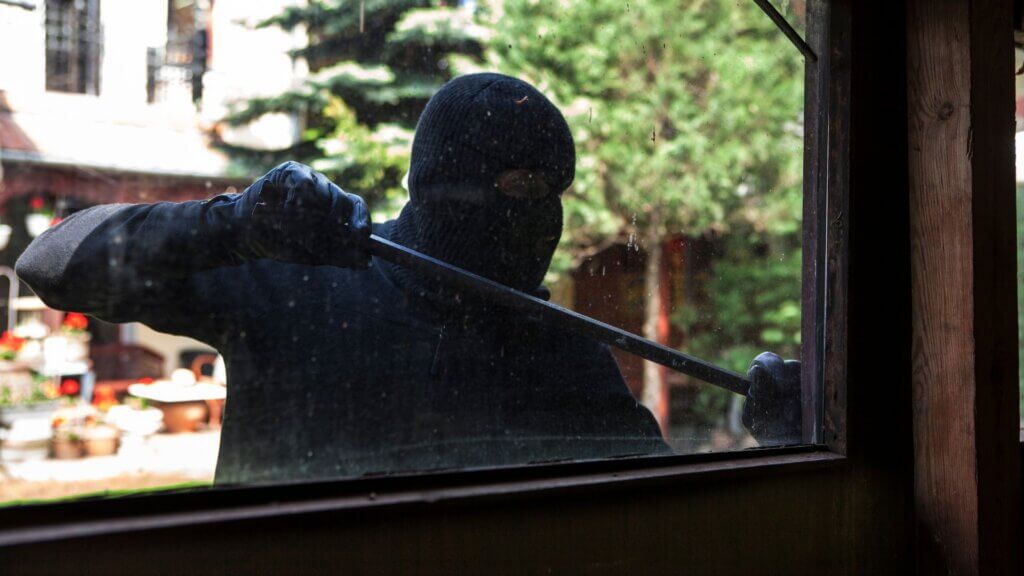 Masked intruder using a pry bar to force open a window.