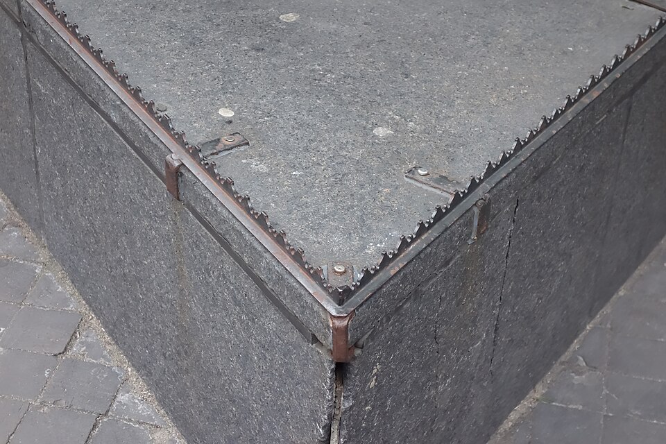 Close-up of metal anti-homeless spikes installed along the edge of a raised concrete ledge, designed to prevent people from sitting or lying down in a public space.
