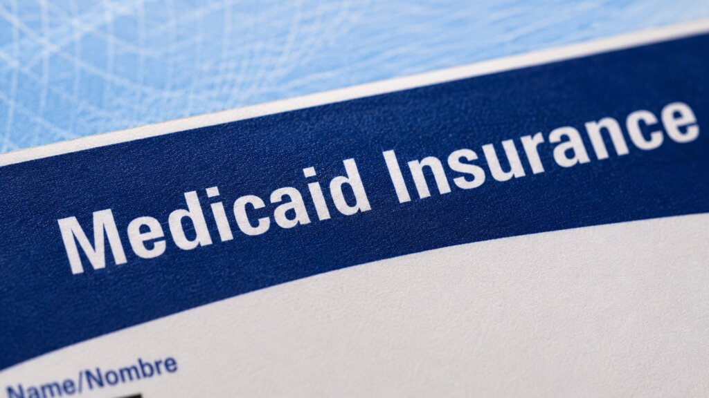 Close up of a Medicaid insurance document with the text "Medicaid Insurance" printed in large white letters on a blue header.